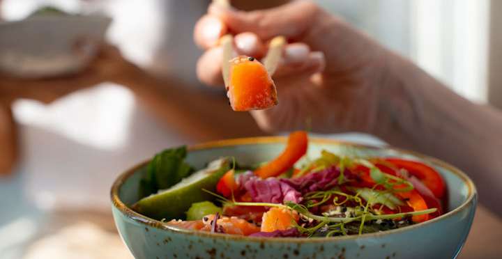 Mão segurando um tomate sobre uma tigela de salada