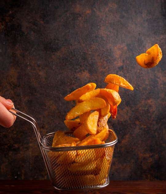 Batatas fritas caindo em cesto de fritura