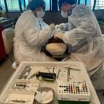Dentistas paramentados realizam procedimento cirúrgico com bandeja de instrumentos estéreis