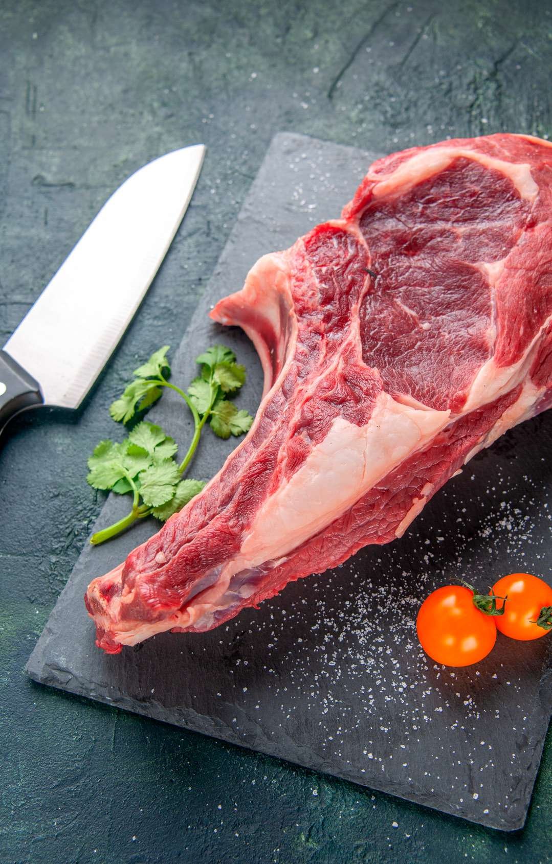 Corte de carne crua sobre tábua com faca e tomates