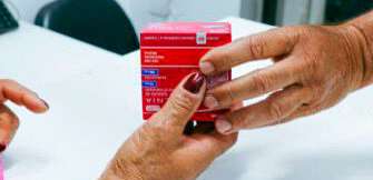 Mãos entregando uma caixa de medicamento