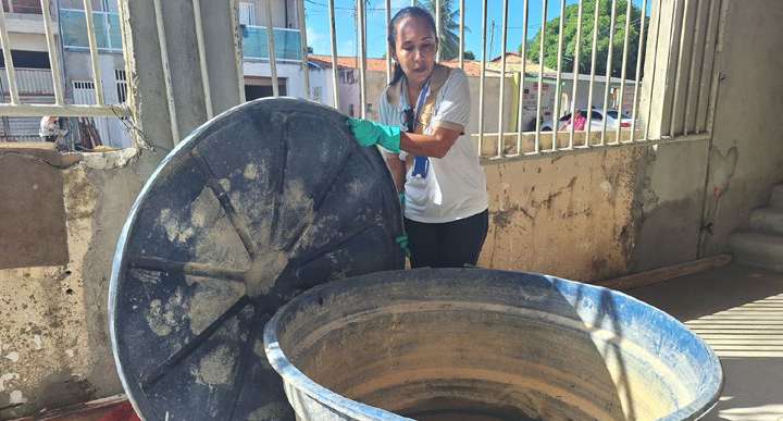 Agente de endemias inspeciona recipiente com água em quintal