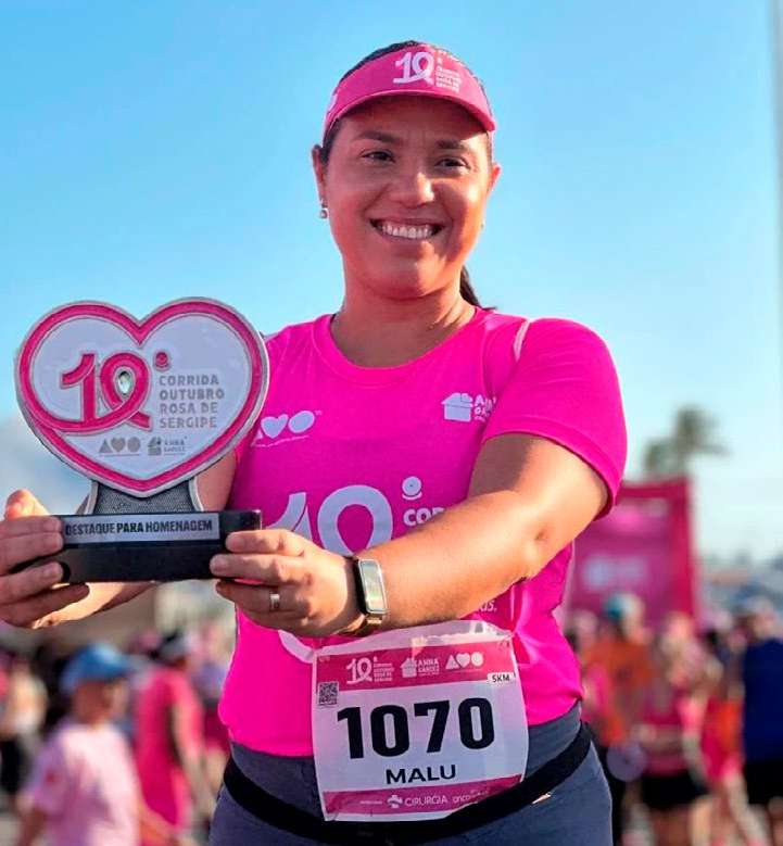 Corredora de camiseta rosa segurando troféu da Corrida Outubro Rosa
