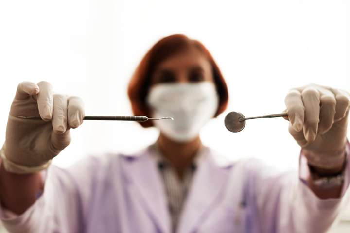 Dentista de máscara segurando espelho e sonda odontológica