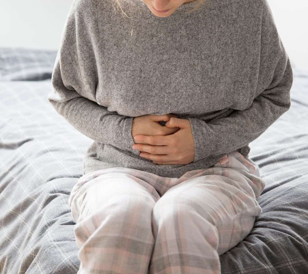 Pessoa com as mãos sobre a barriga, sentada na cama