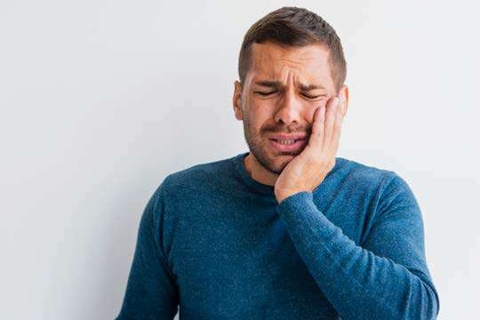 Homem com a mão no rosto sentindo dor de dente