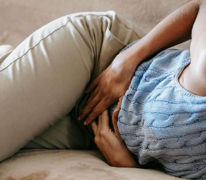 Mulher deitada com as mãos sobre o abdome, com cólica