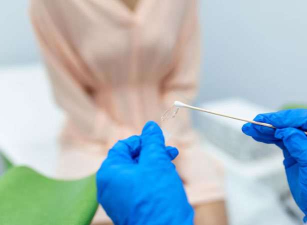 Mãos com luvas manipulando cotonete de coleta de exame