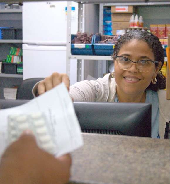 Farmacêutica entrega medicamento no balcão de uma unidade de saúde