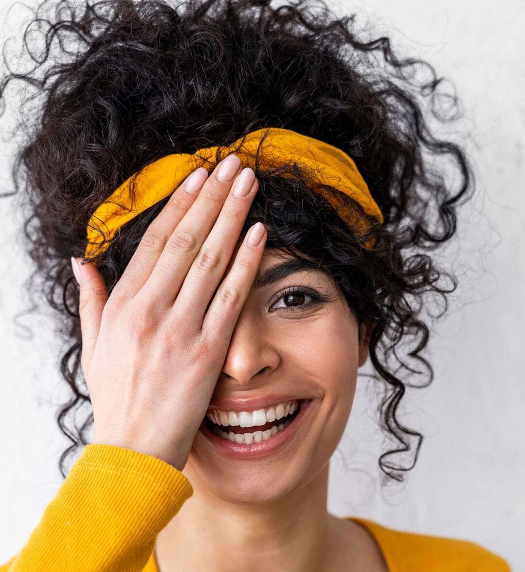 Mulher sorridente com faixa amarela no cabelo cobrindo um dos olhos