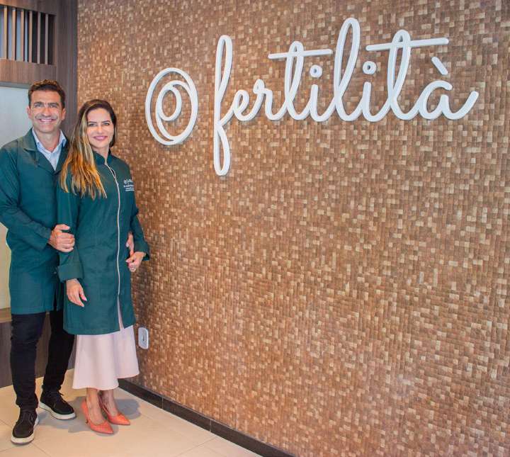 Dr. Iuri Telles e Dra. Andréa Telles diante do painel da Clínica Fertilità