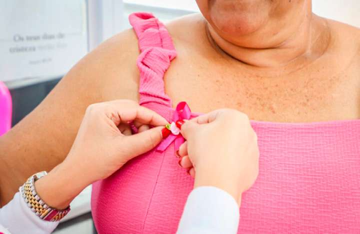 Mãos prendendo um laço rosa na roupa de uma paciente