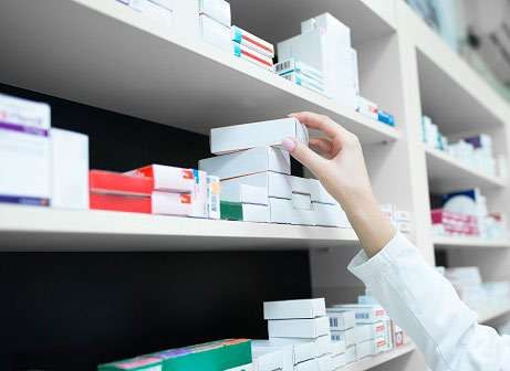 Mão retirando caixa de medicamento de prateleira de farmácia