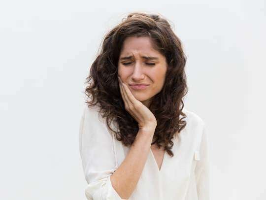 Mulher com a mão no rosto sentindo dor de dente