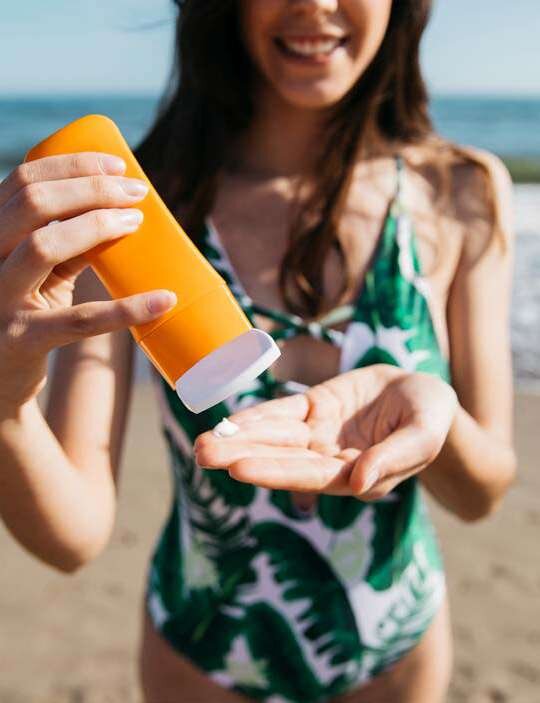 Mulher na praia segura frasco de protetor solar