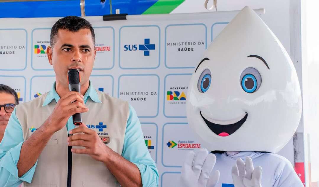 Tiago Rangel fala ao microfone ao lado do mascote Zé Gotinha