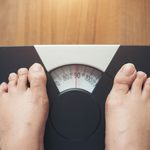 Woman feet standing on Weight Scale on wooden background